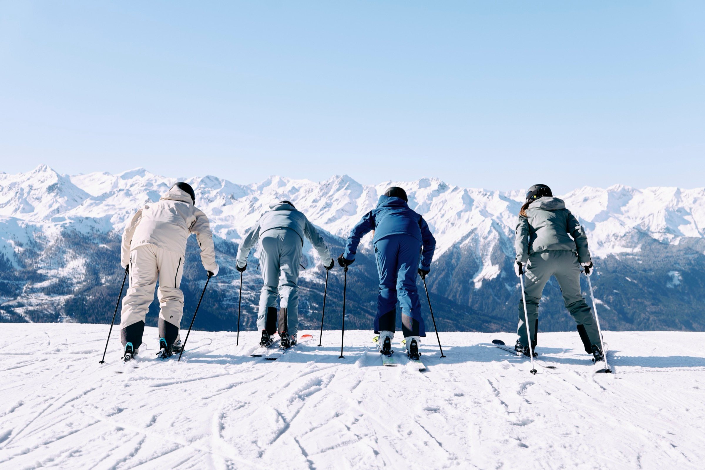 Vier Skifahrer in aktueller Skibekleidung vor Bergpanorama — Wintermode wie bei INTERSPORT Ladner in Kappl