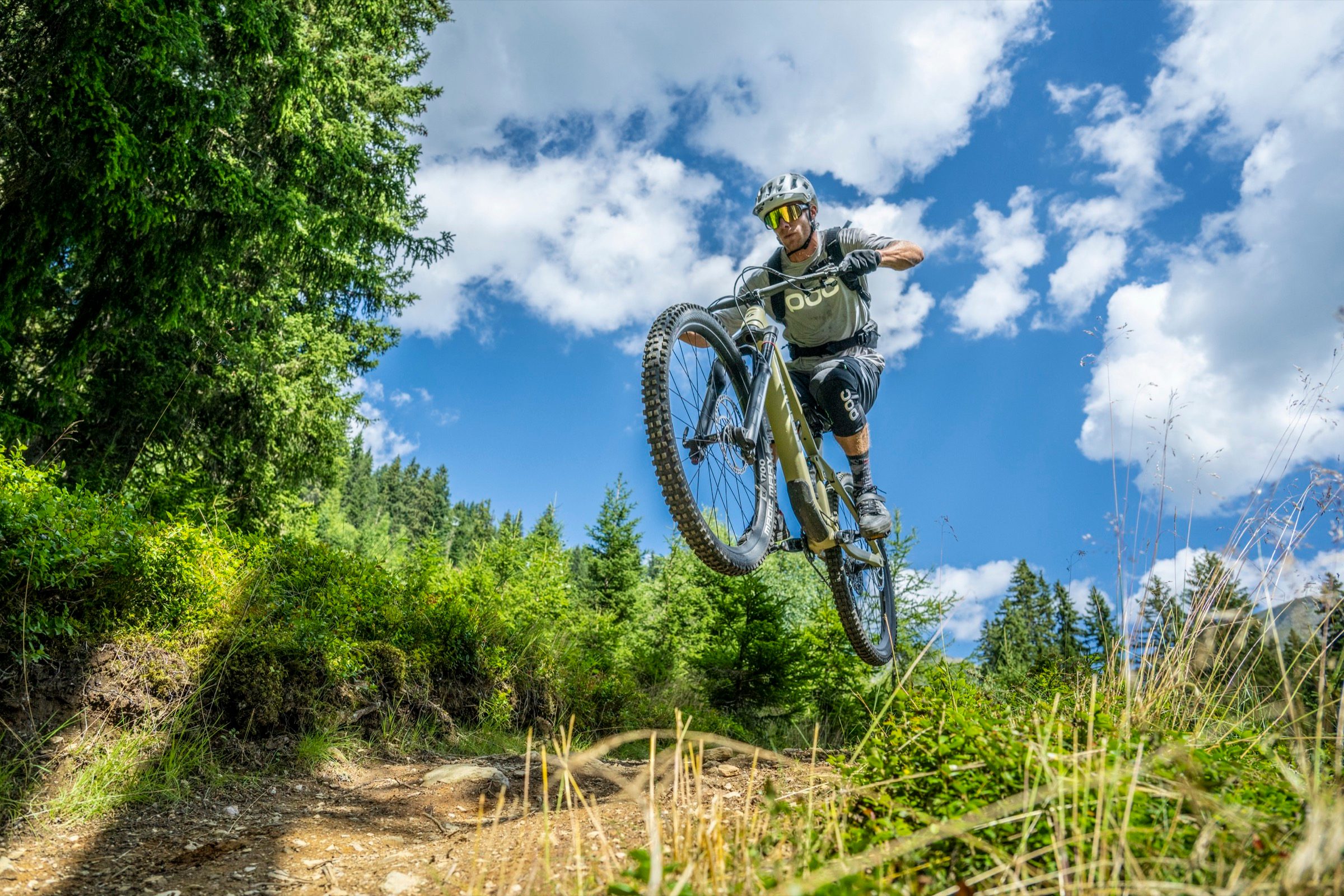 Ein Mountainbiker springt über einen Trail-Kicker im Wald über Kappl