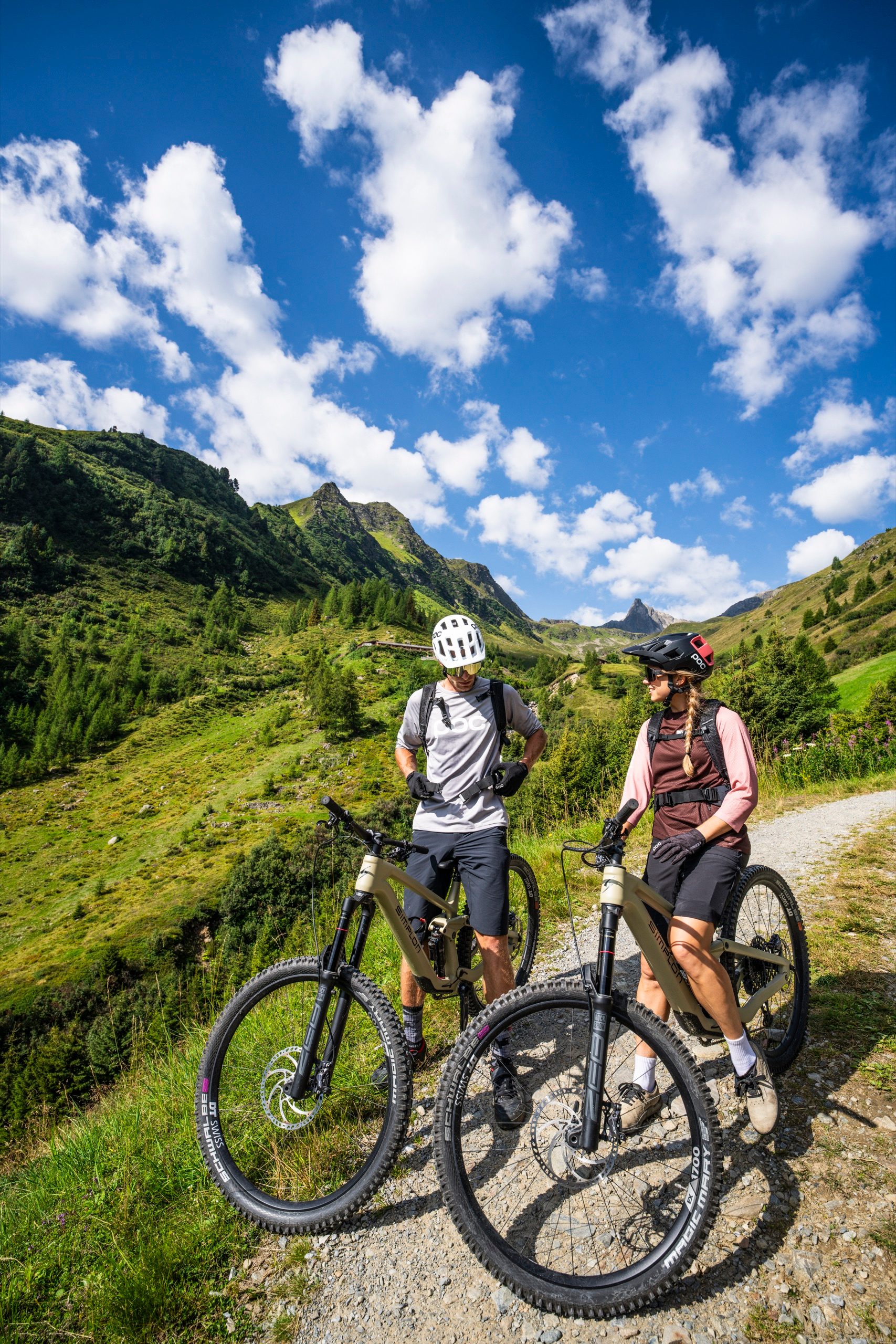Zwei Mountainbiker stehen mit ihren E-MTBs auf einem Trail über Kappl, dahinter grüne Berghänge