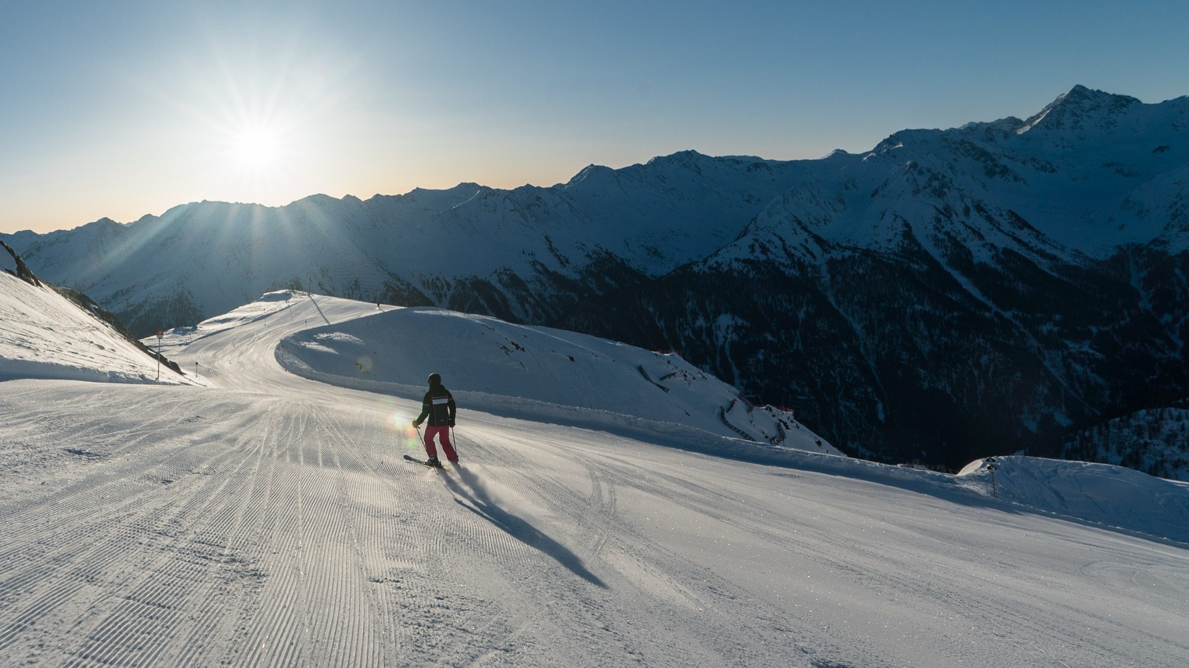Ein Skifahrer zieht im Sonnenaufgang seine Schwünge auf präparierter Piste hoch über Kappl