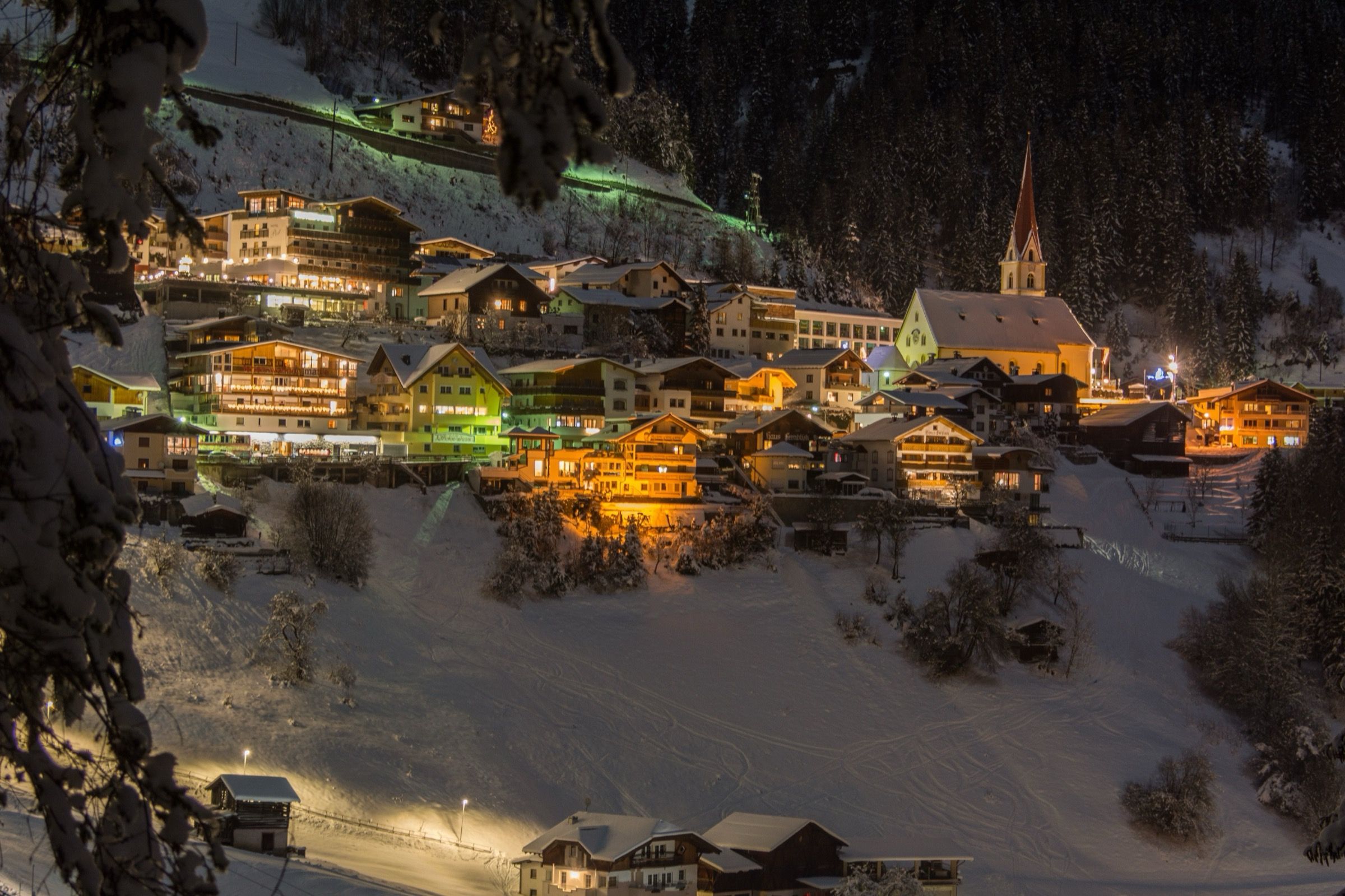 Kappl bei Nacht — das beleuchtete Dorf im Schnee, der Kirchturm vor den dunklen Paznauner Hängen